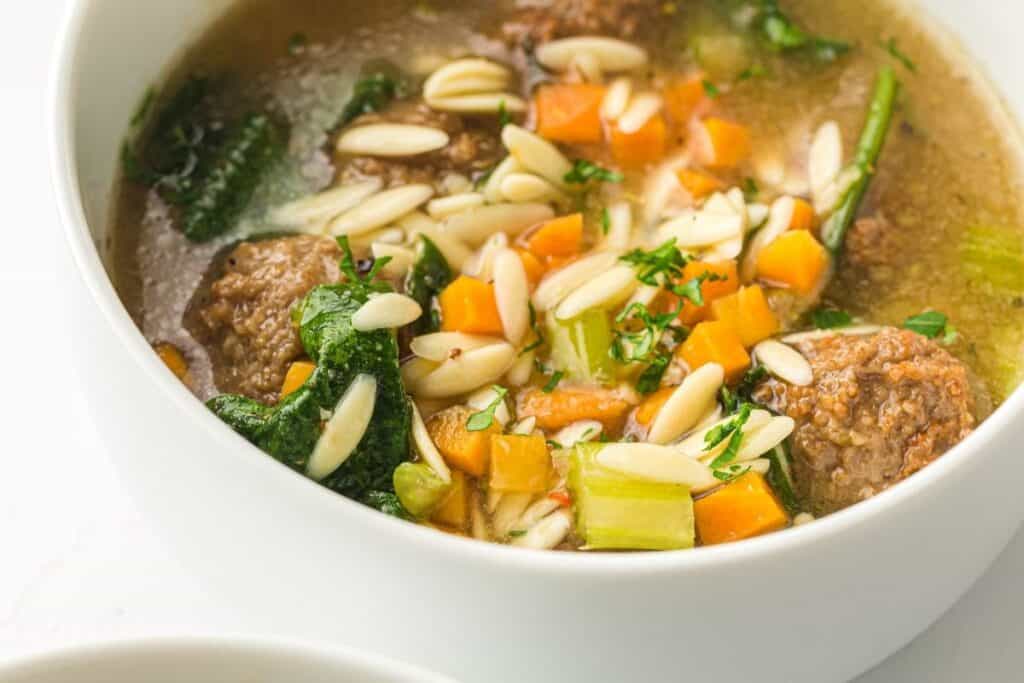 A bowl of soup with meatballs, sliced almonds, spinach, chopped carrots, celery, and broth.