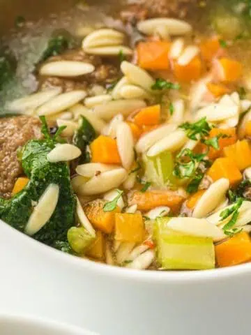 A close-up of a spoon holding a meatball in a bowl of Slow Cooker Italian Wedding Soup.