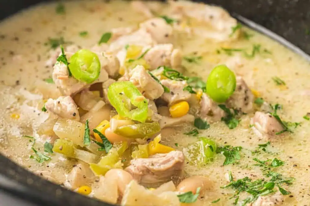 A close-up of a bowl of white chicken chili with pieces of chicken, white beans, corn, green peppers, and chopped herbs in a creamy broth.