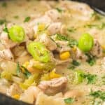 A close-up of a bowl of white chicken chili with pieces of chicken, white beans, corn, green peppers, and chopped herbs in a creamy broth.