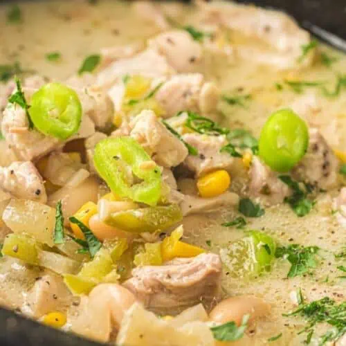A close-up of a bowl of white chicken chili with pieces of chicken, white beans, corn, green peppers, and chopped herbs in a creamy broth.