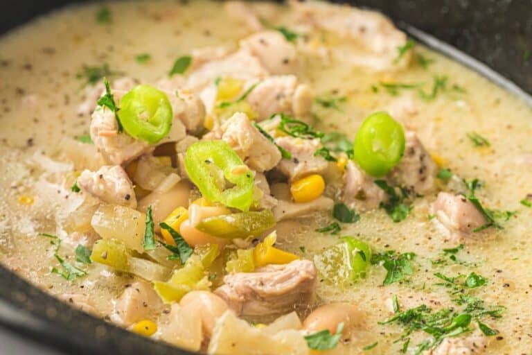 A close-up of a bowl of white chicken chili with pieces of chicken, white beans, corn, green peppers, and chopped herbs in a creamy broth.