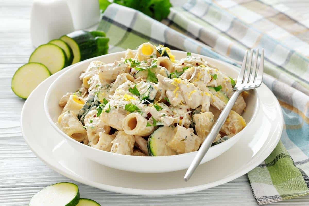 A bowl of Zucchini & Chicken Alfredo, served with a fork on a white plate.