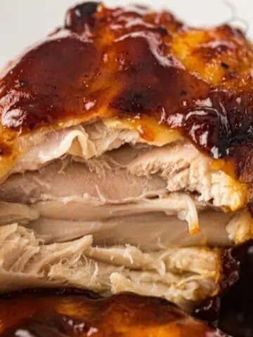 Close-up of a piece of barbecued chicken with a bite taken out, showing the inside texture and barbecue sauce coating.