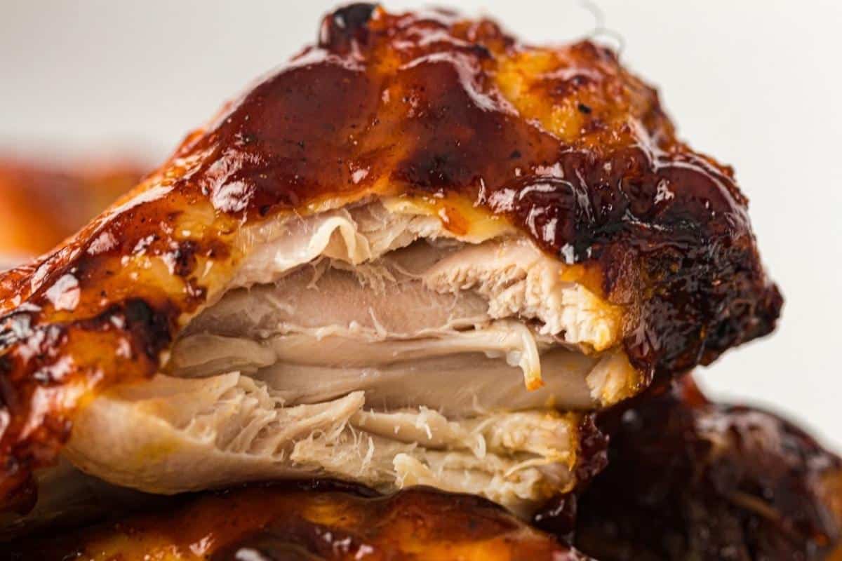 Close-up of a piece of barbecued chicken with a bite taken out, showing the inside texture and barbecue sauce coating.