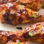 Close-up of baked chicken drumsticks coated in barbecue sauce and garnished with chopped parsley on a white plate.