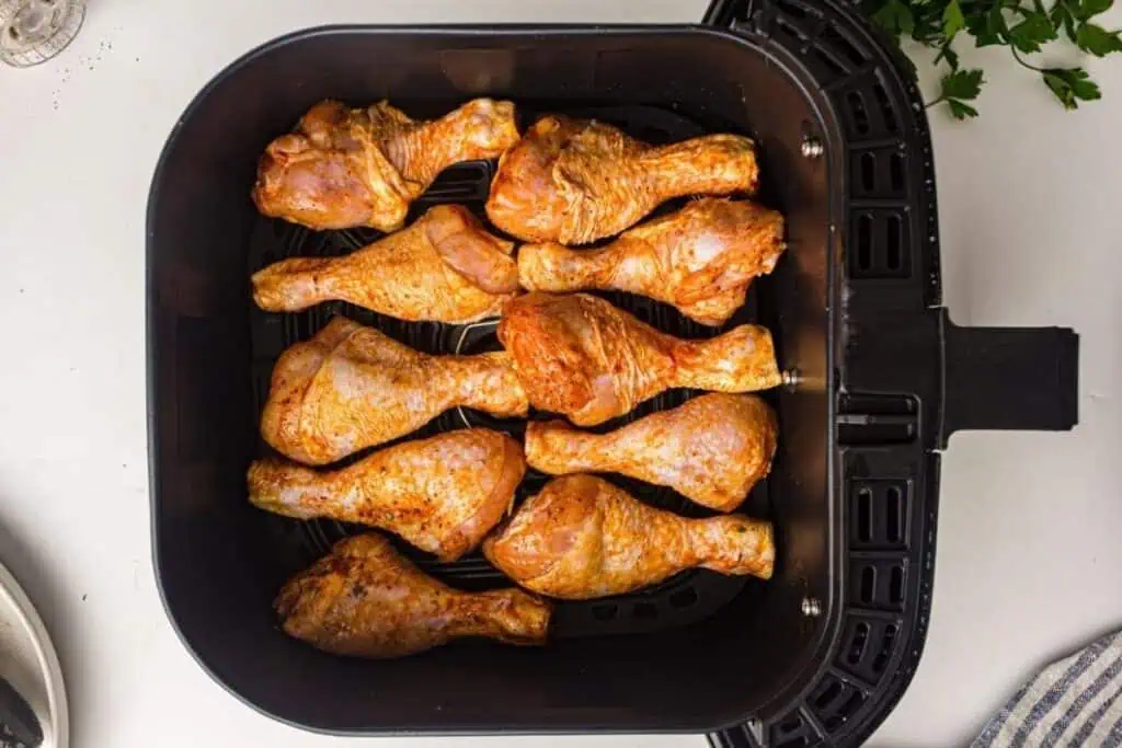 Nine seasoned chicken drumsticks arranged in a single layer inside an air fryer basket, ready for cooking.