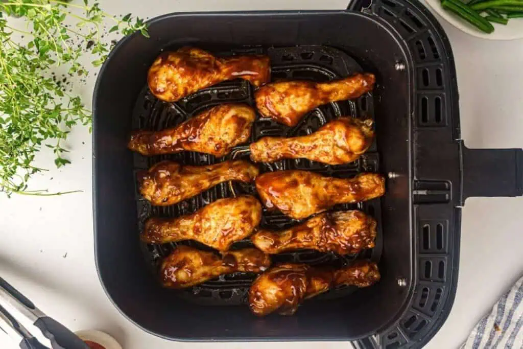 Nine glazed chicken drumsticks arranged in a single layer inside an air fryer basket, ready to be cooked.