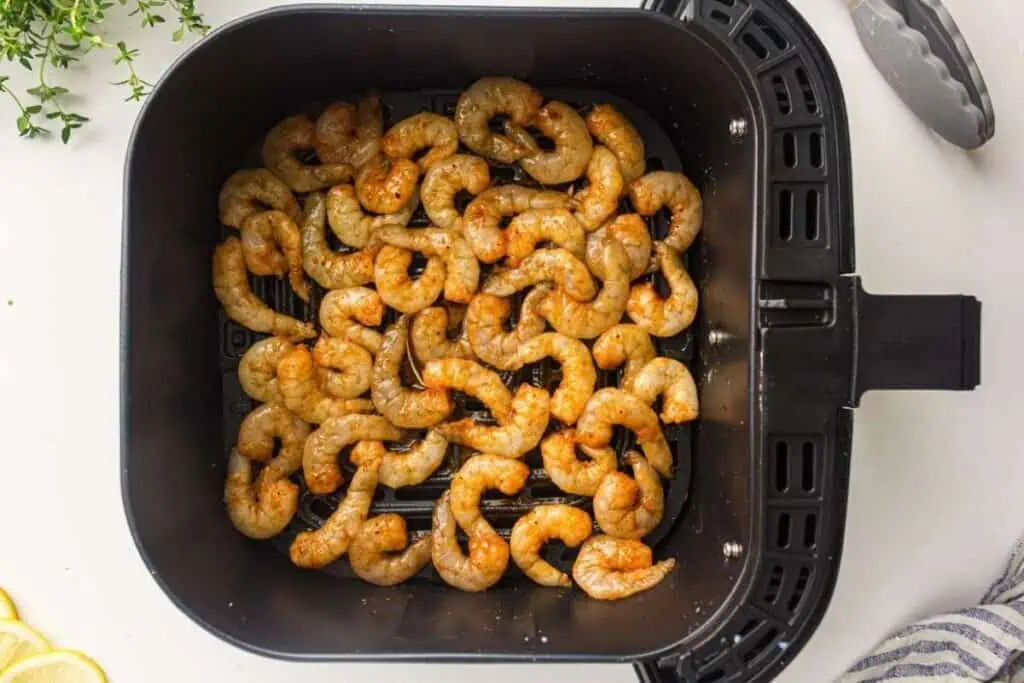 Raw seasoned shrimp arranged in a single layer inside an air fryer basket, ready for cooking.