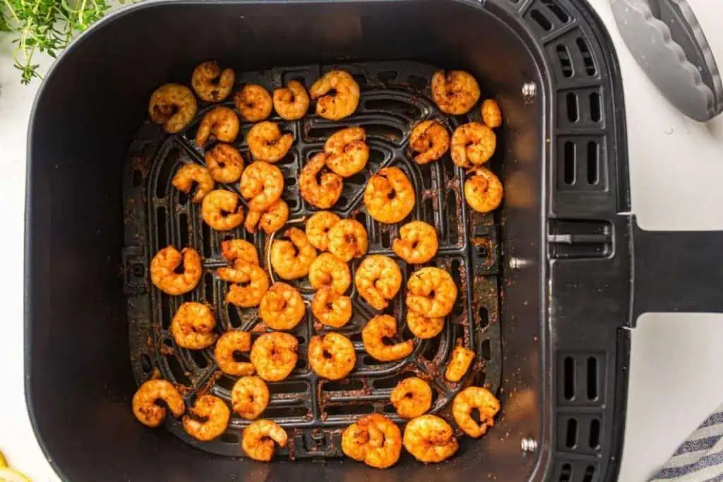 Cooked, seasoned shrimp arranged inside an air fryer basket.