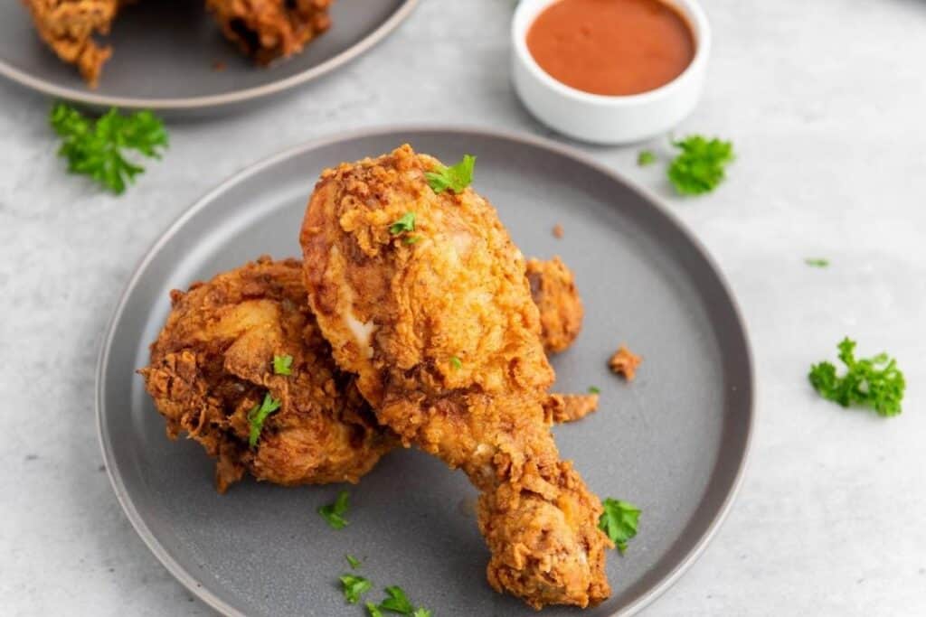 Two pieces of fried chicken garnish with parsley on a gray plate, with a small bowl of dipping sauce in the background.