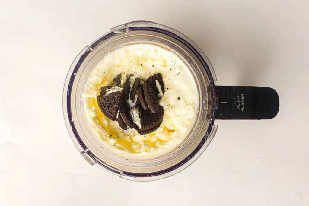 A blender filled with a creamy mixture and broken chocolate sandwich cookies on top, viewed from above.