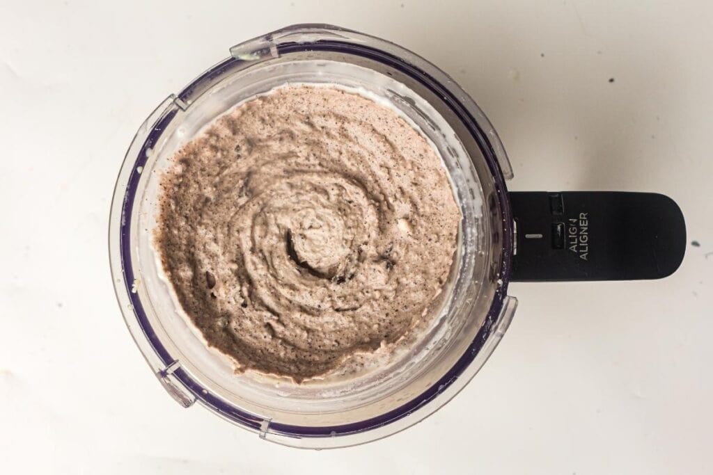 A food processor bowl containing a thick, blended mixture with a speckled, creamy texture viewed from above.