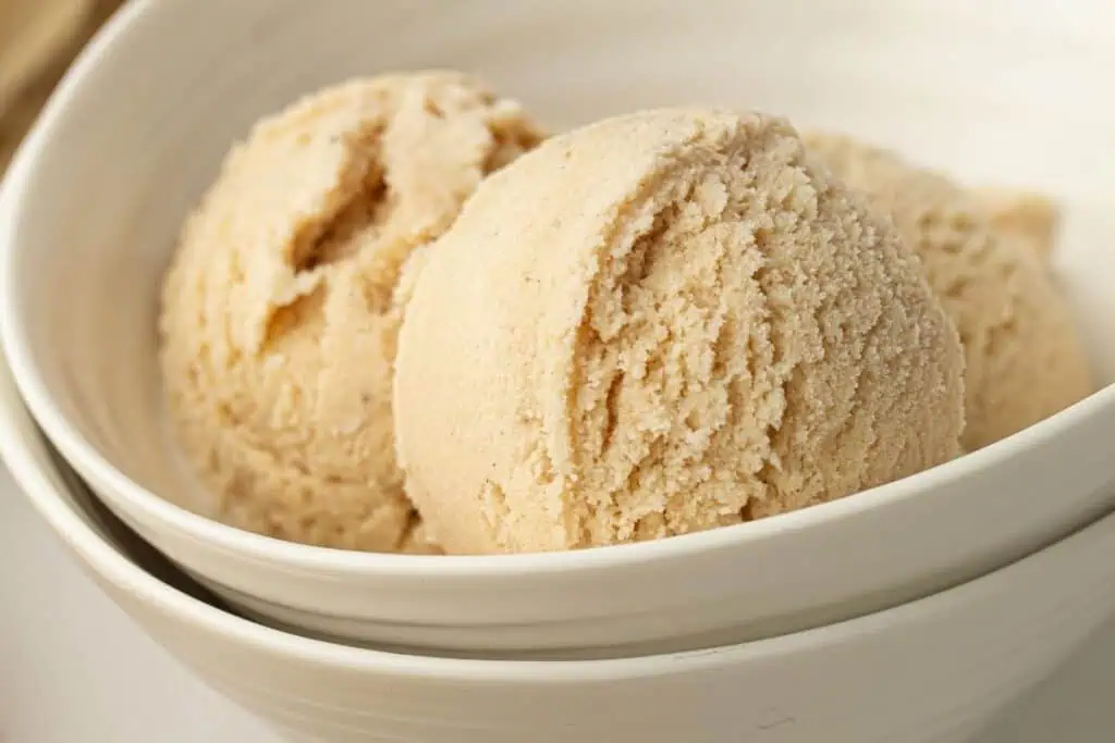 Two scoops of light brown ice cream in a white bowl, with a second bowl partially visible underneath.