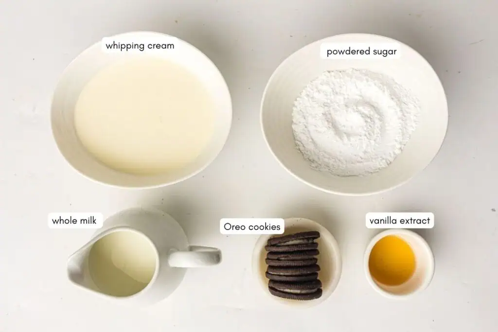 Five labeled bowls and containers hold whipping cream, powdered sugar, whole milk, Oreo cookies, and vanilla extract on a white background.