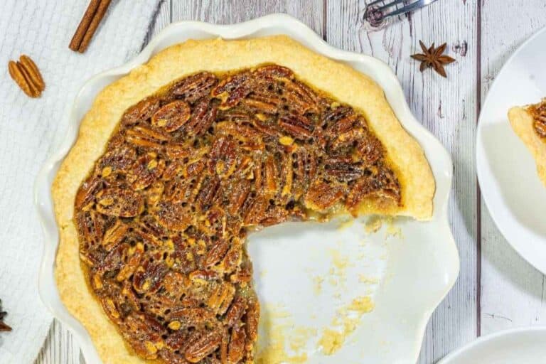 A pecan pie in a white pie dish with a large slice missing, showing the filling and crust.