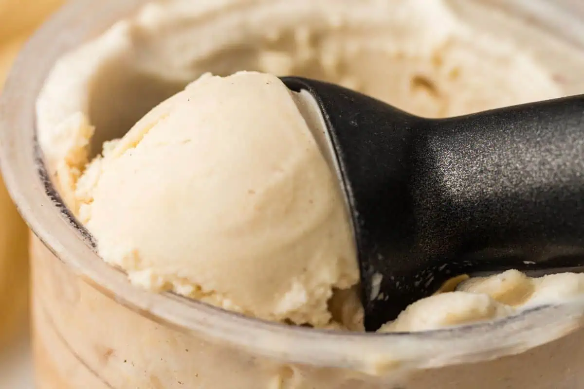 A close-up of a black ice cream scoop lifting vanilla ice cream from a container.