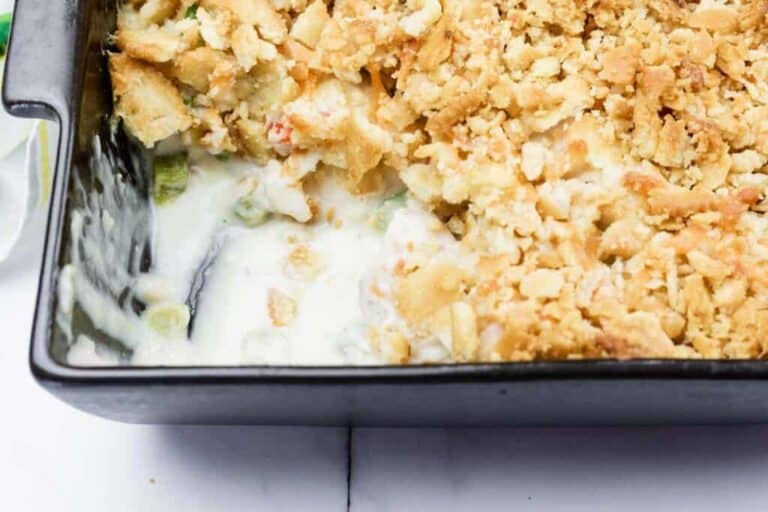A casserole dish filled with a creamy mixture and topped with a golden, crumbly crust, with a portion scooped out.