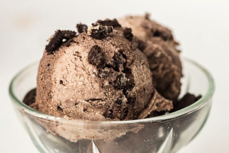 Two scoops of chocolate ice cream with cookie pieces in a glass bowl.