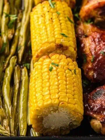 Roasted baby potatoes, green beans, corn on the cob, and barbecue chicken arranged on a tray.