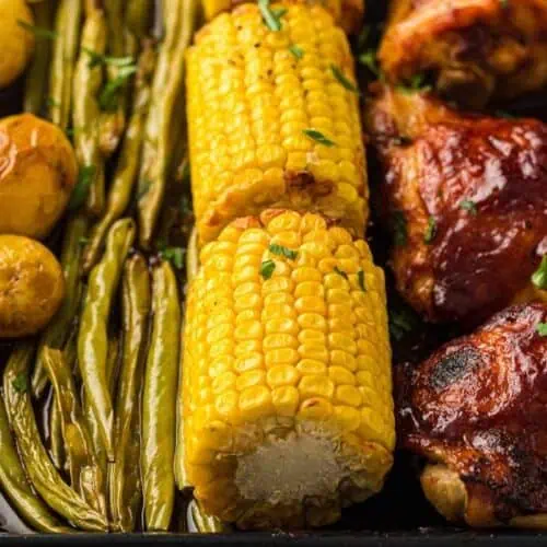 Roasted baby potatoes, green beans, corn on the cob, and barbecue chicken arranged on a tray.