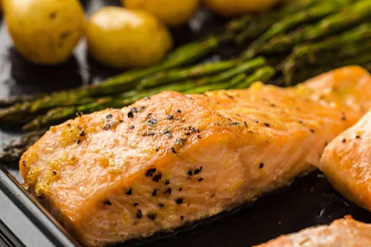 Close-up of a baked salmon fillet seasoned with pepper, served alongside asparagus spears and small roasted potatoes.