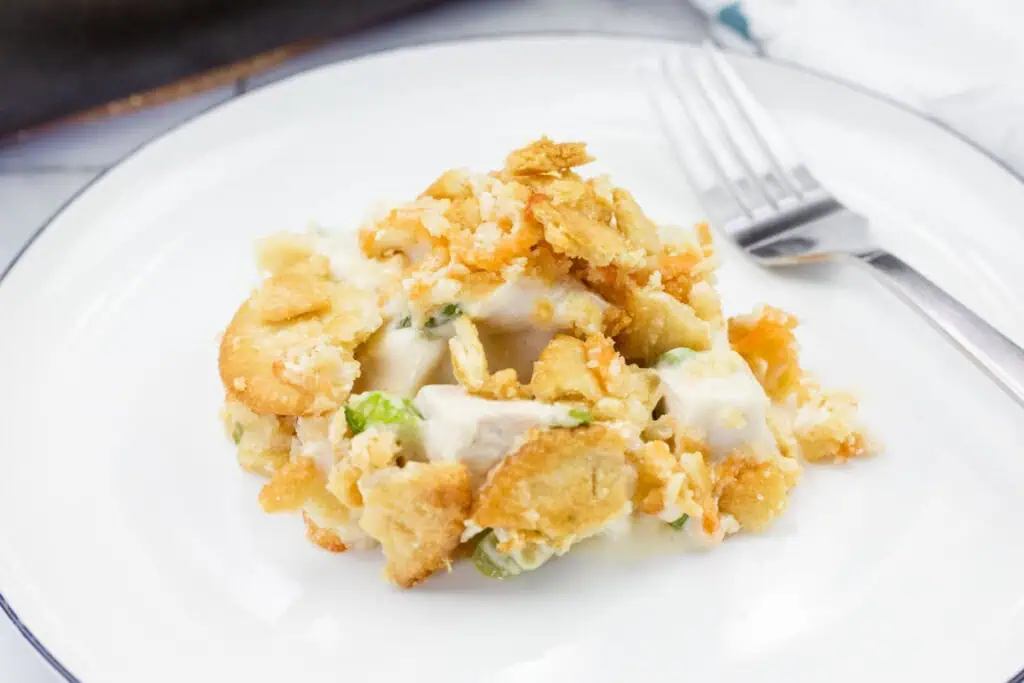 A serving of Cheesy Ritz Cracker Chicken Casserole sits on a white plate next to a fork.