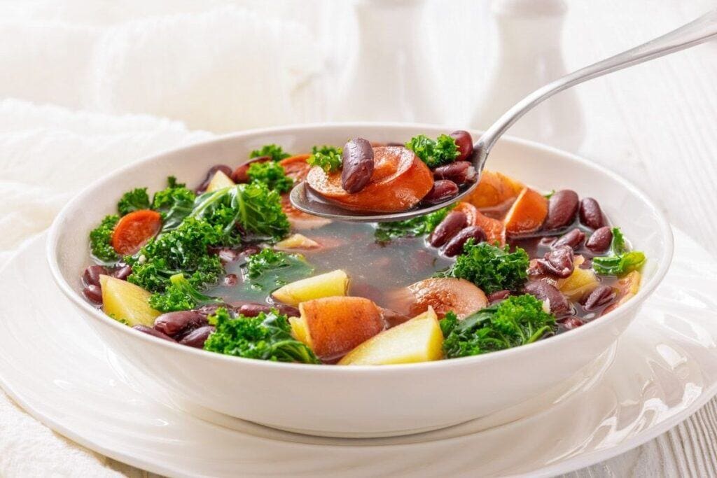 A bowl of Sausage & Kale Soup with a spoon lifting a portion from the bowl.