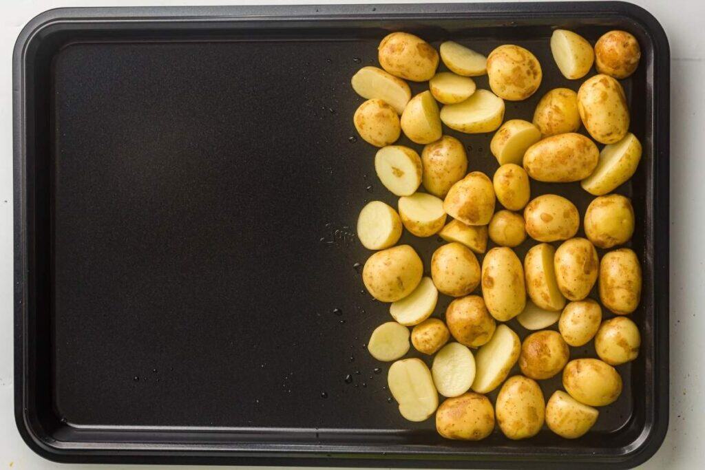 A baking sheet with halved and whole small potatoes arranged on one side; the other side of the tray is empty.