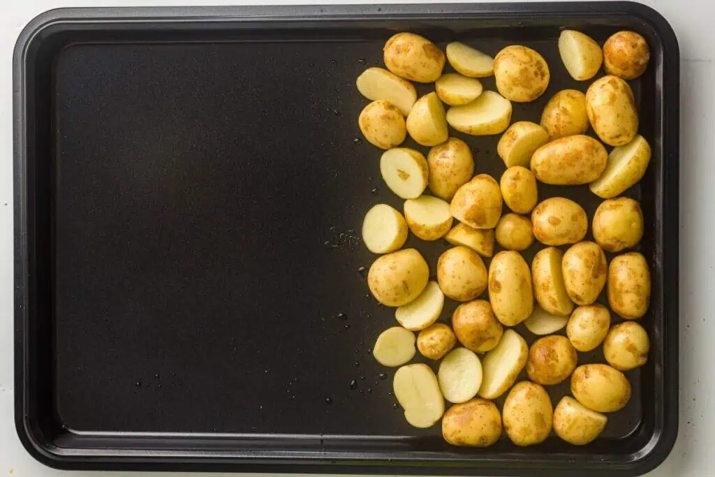 A baking sheet with halved and whole small potatoes arranged on one side; the other side of the tray is empty.