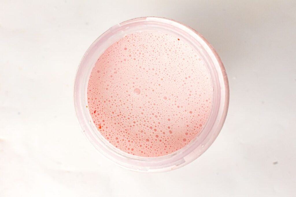 A top-down view of a cup filled with a pink, frothy liquid on a white surface.