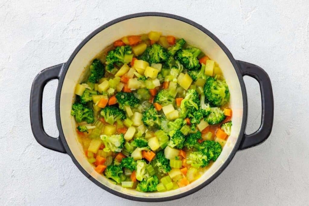 A pot of vegetable soup with broccoli, carrots, celery, and potatoes in broth, viewed from above.