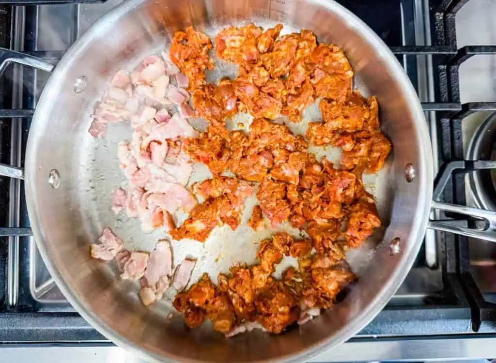 Raw bacon and seasoned ground meat are cooking in a stainless steel pan on a stovetop.