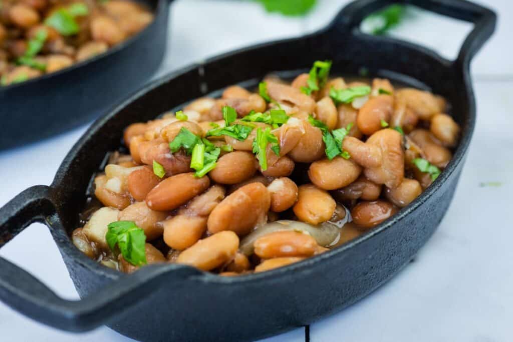 A black oval dish filled with cooked pinto beans, garnished with chopped fresh herbs.
