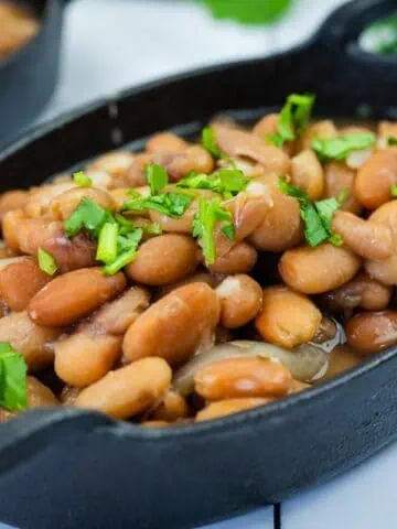 A black oval dish filled with cooked pinto beans, garnished with chopped fresh herbs.
