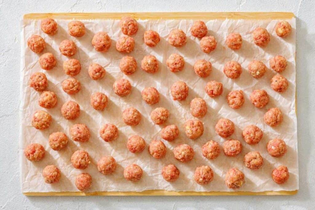 Raw meatballs arranged in neat rows on a parchment-lined baking sheet.