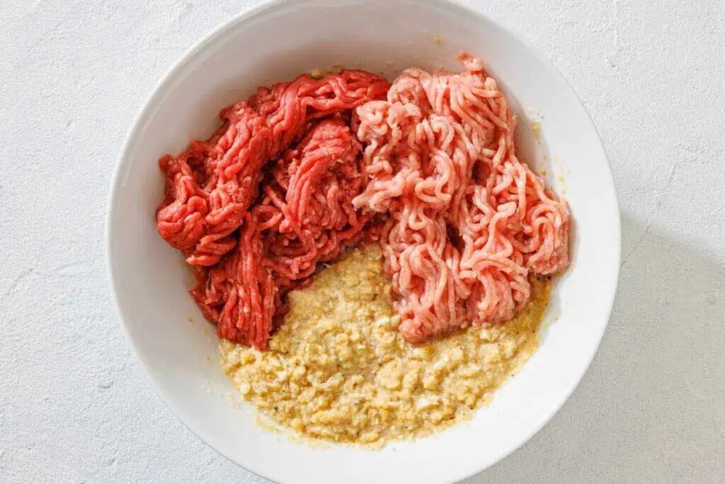A white bowl containing ground beef, ground pork, and a mixture of breadcrumbs and eggs.