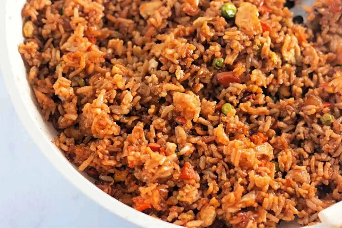 A close-up of a plate of fried rice mixed with vegetables, small pieces of meat, and a savory brown sauce.