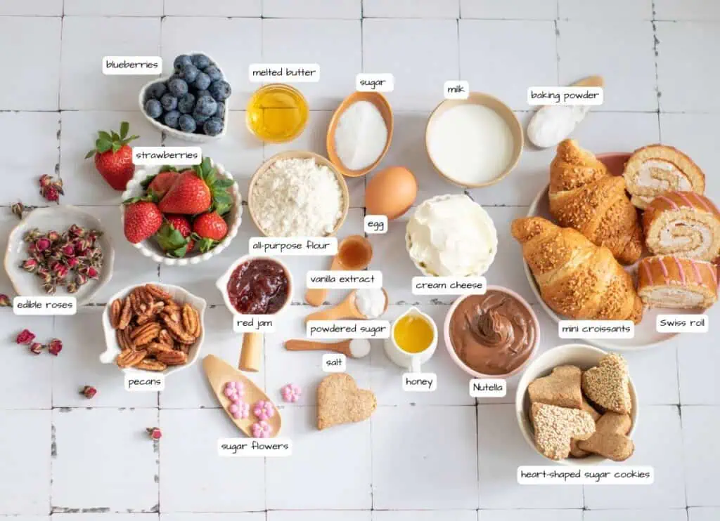A variety of baking ingredients and treats, including eggs, flour, fruits, nuts, spreads, cookies, mini croissants, Swiss roll, and labeled containers, arranged on a white surface.