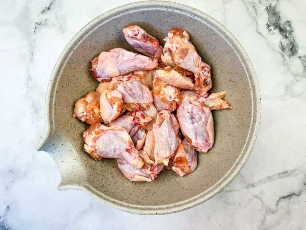 A gray bowl filled with raw, cut chicken wings sits on a marble countertop.