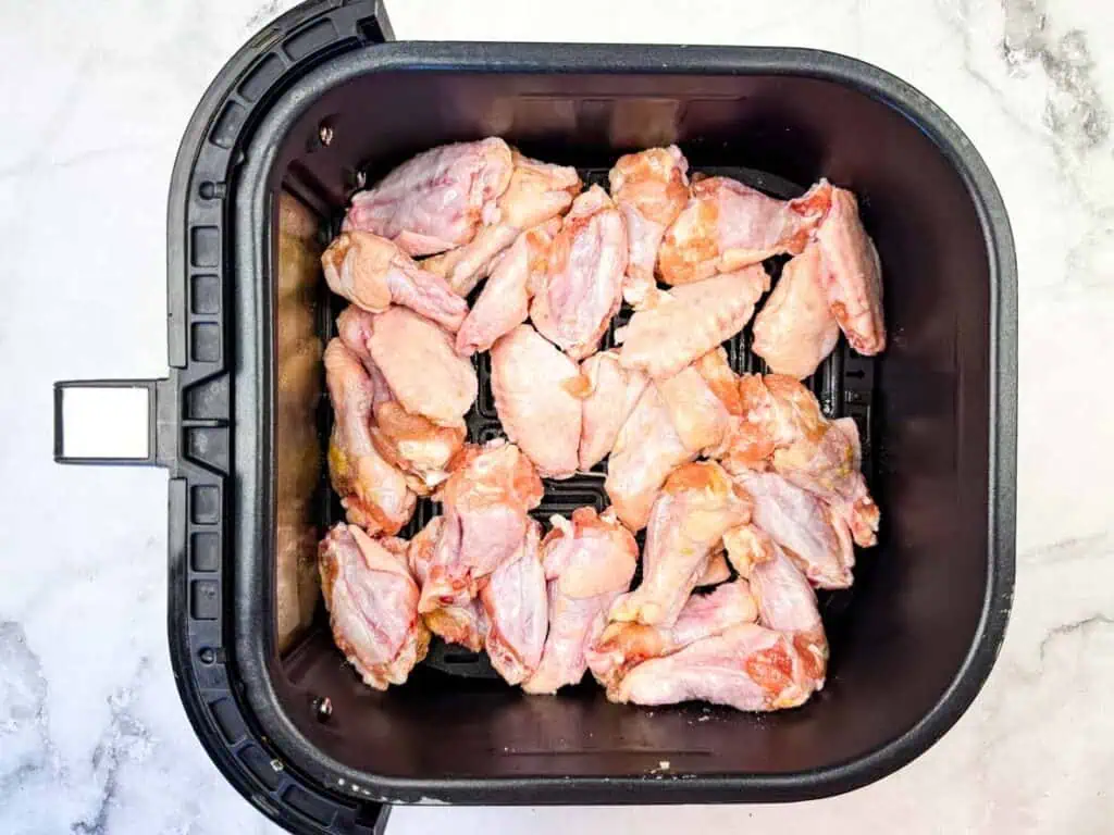 Raw chicken wings arranged in a single layer inside the basket of an air fryer on a white countertop.