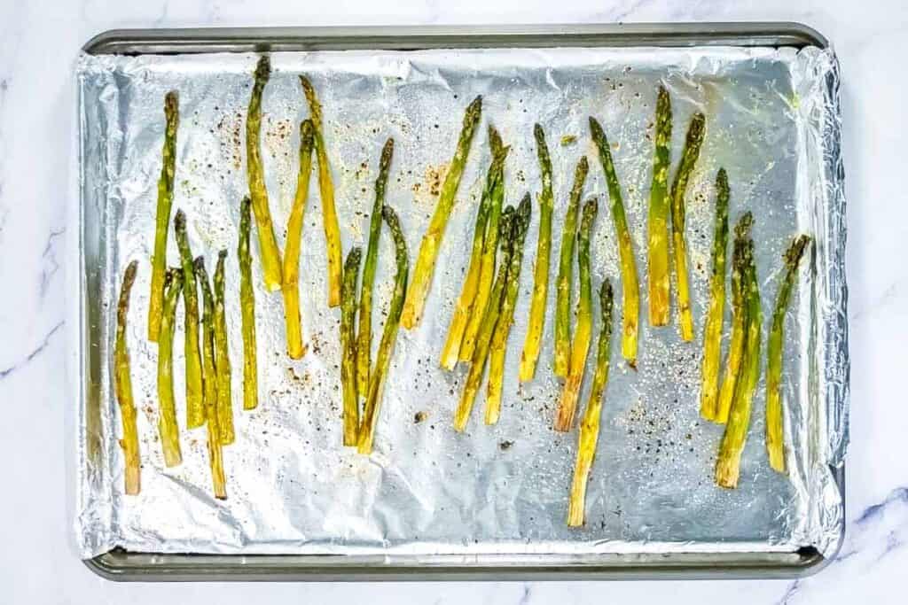 Roasted asparagus spears arranged on a foil-lined baking sheet, seasoned with pepper and lightly browned.