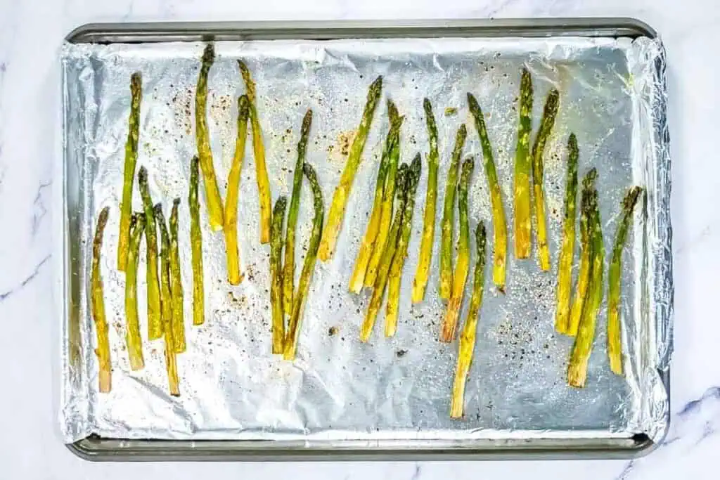 Roasted asparagus spears arranged on a foil-lined baking sheet, seasoned with pepper and lightly browned.