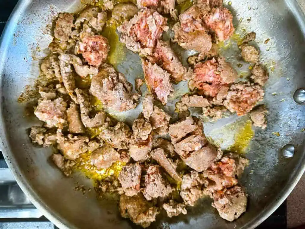 Ground beef partially browned and cooking in a stainless steel skillet with oil.