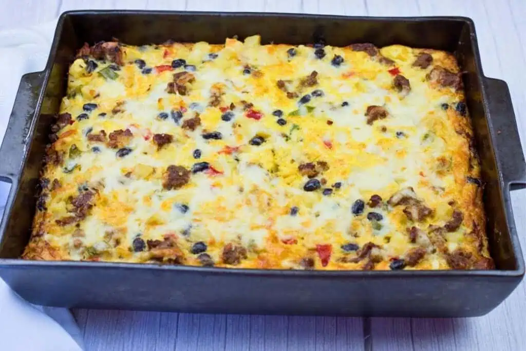 Rectangular casserole dish filled with a baked egg and cheese breakfast casserole containing vegetables, sausage, and black beans.