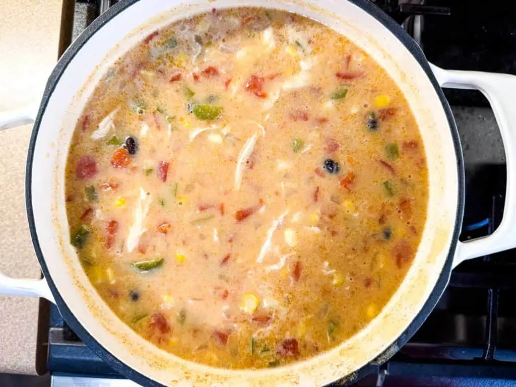 A pot of soup with shredded chicken, corn, black beans, tomatoes, and green peppers simmering on a stove.