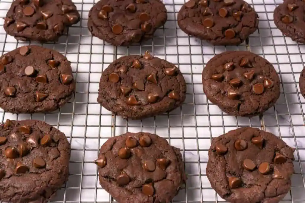 Rows of chocolate chip cookies cooling on a metal wire rack, with visible chocolate chips on top of each cookie.