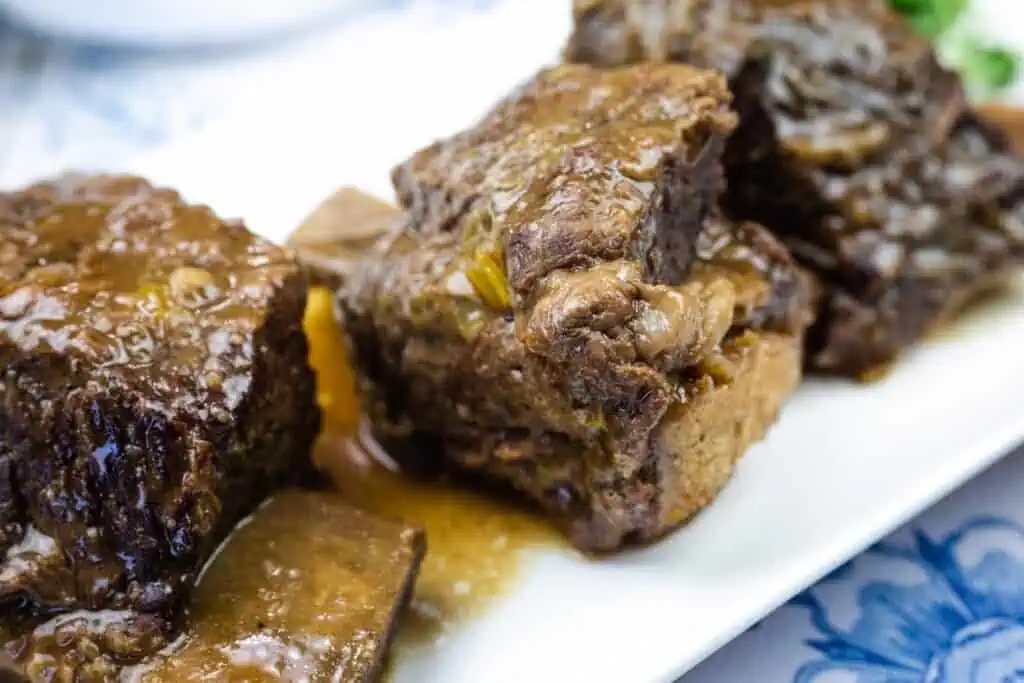 Three pieces of braised beef short ribs with sauce served on a white plate.