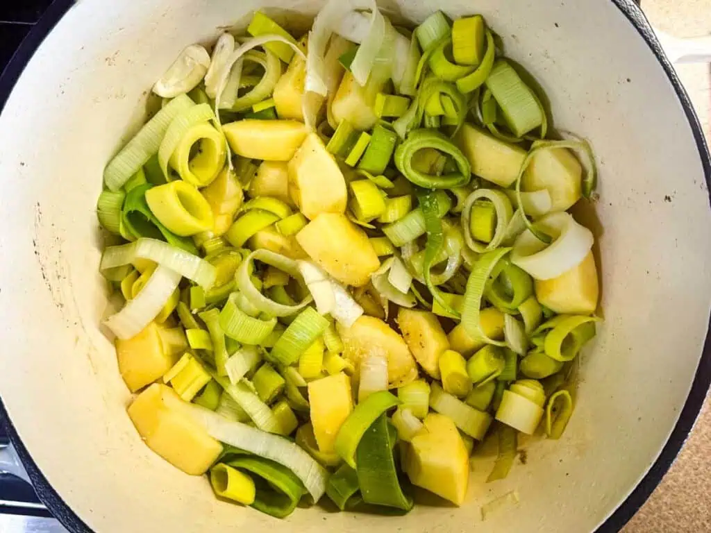 Chopped leeks and potatoes cooking in a white pot.