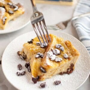 A plate with two slices of bread pudding topped with powdered sugar and raisins.